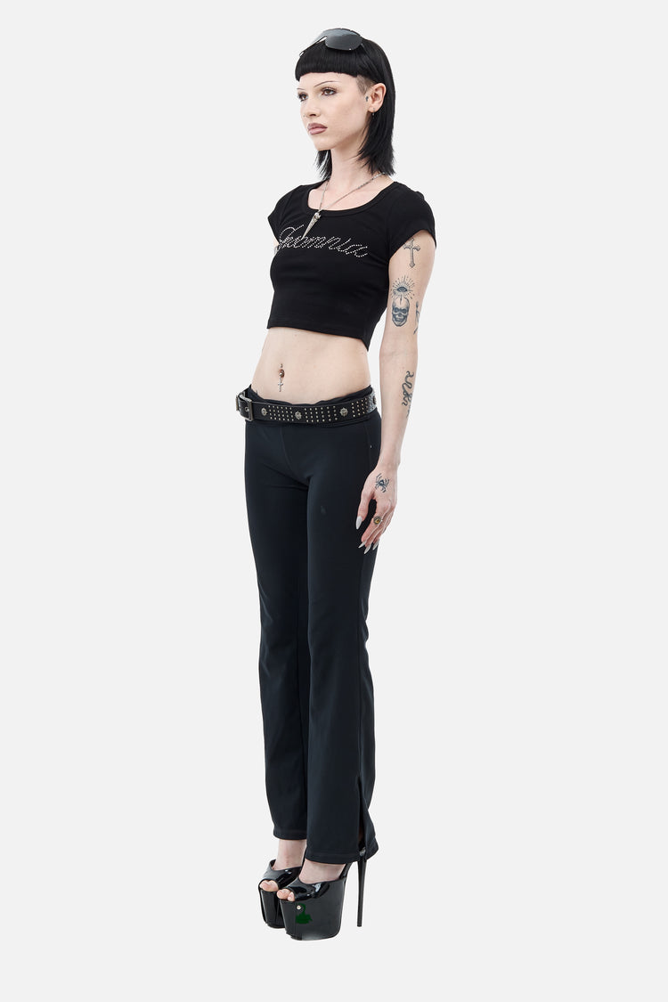 Side view of the cropped Rhinestone Cursive Tee worn with black flared pants and platforms