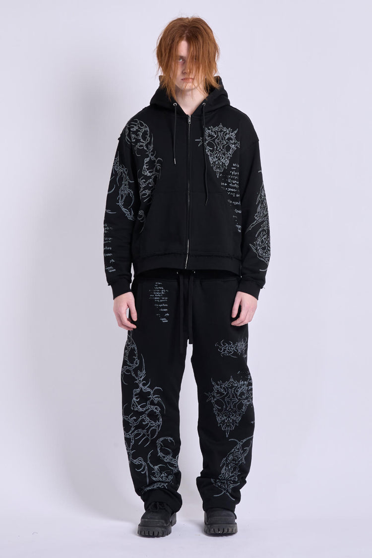 Model wearing the Sigil Sweatpants with a matching black embroidered zip hoodie, full-length front view