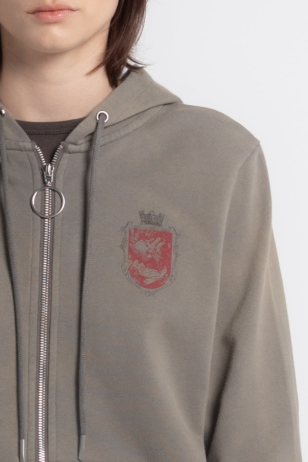 Close-up of the red crest emblem and ring zipper pull on the grey Crest Slim Zip Hoodie
