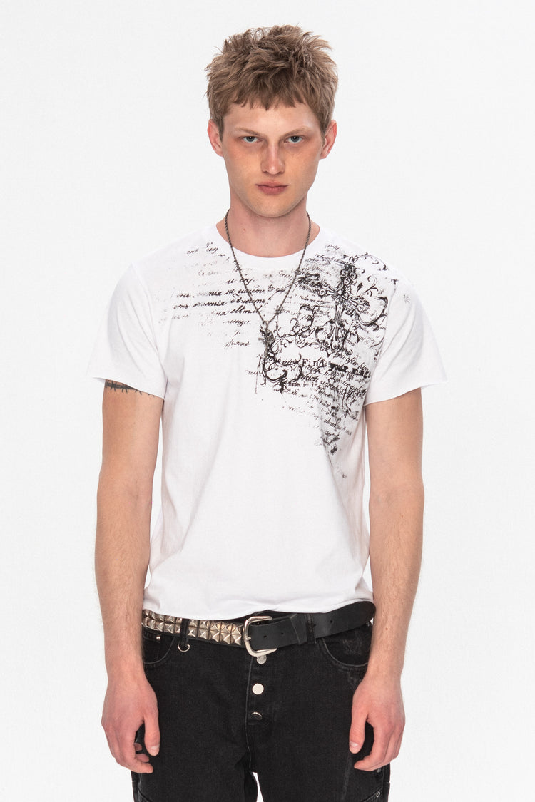 Model wearing the white Orison Tee with black script and cross print on one shoulder