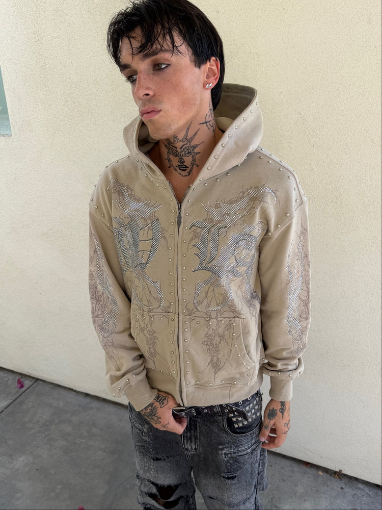 Tattooed model wearing the sand IVLA Zip Up Hoodie with grey gothic IVLA lettering