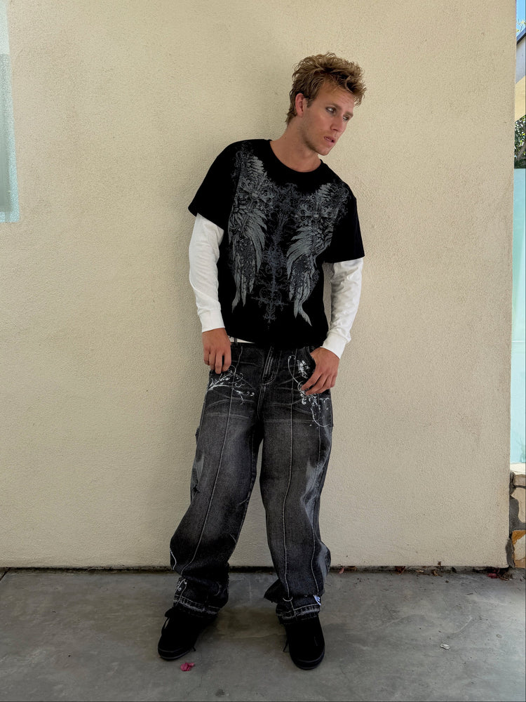 Model leaning on a wall in the grey Fleur Destroyer Denim V2 and wing tee