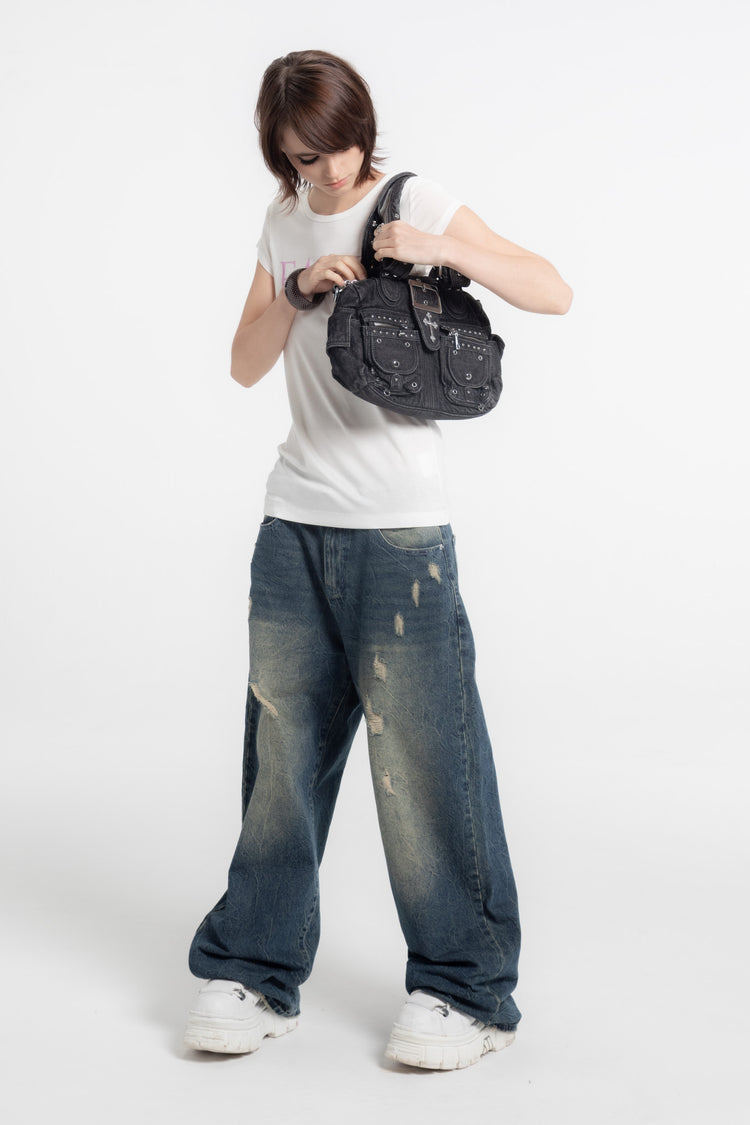 Full-length view of a model opening the Cross Denim Shoulder Bag, white tee and jeans