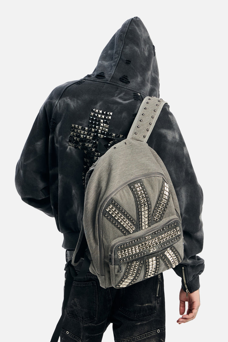 Back view of a hooded model wearing the Studded Flag Backpack on one shoulder