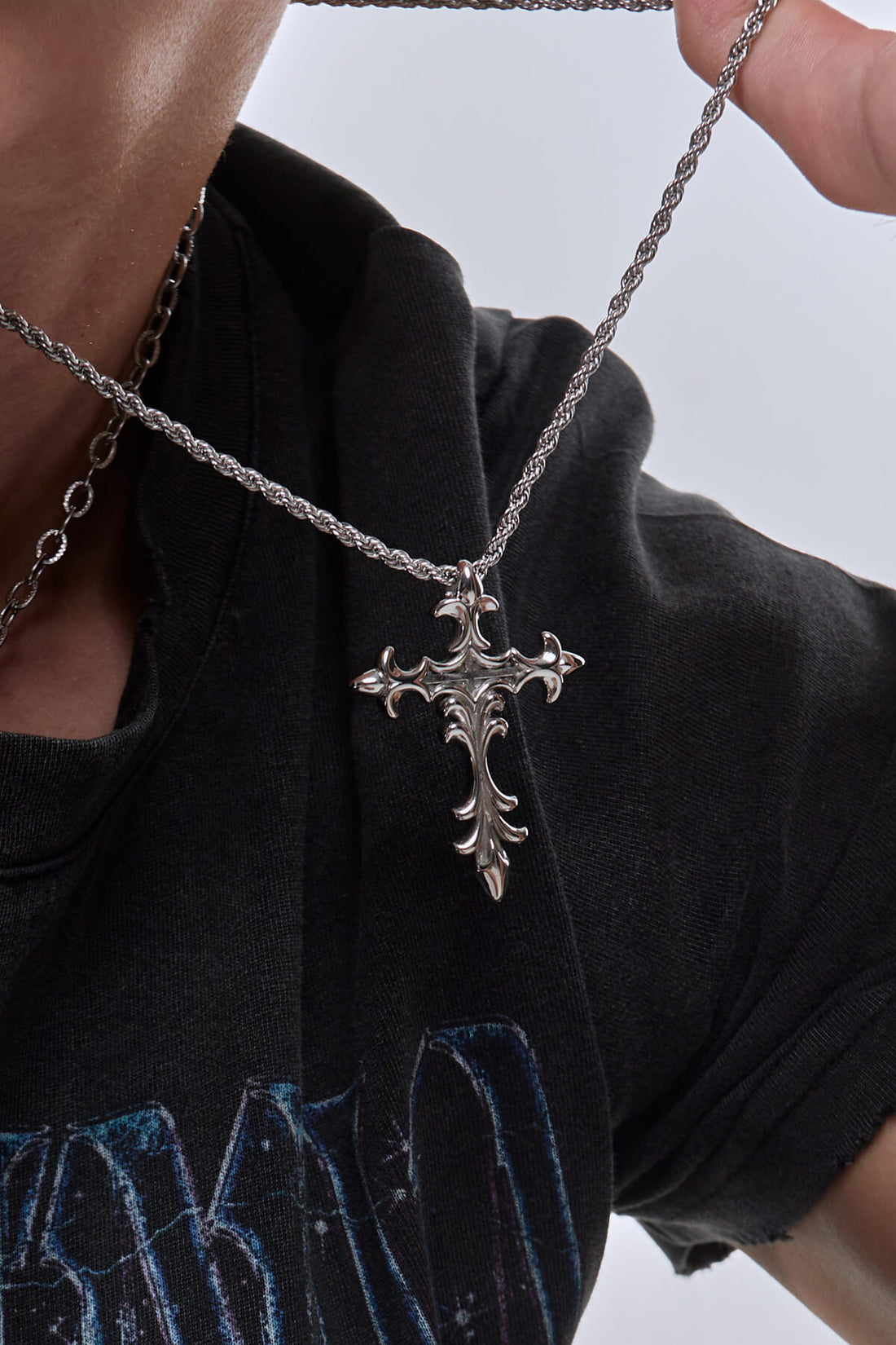 Close-up of the Cross Necklace pendant held out on its rope chain over a black tee