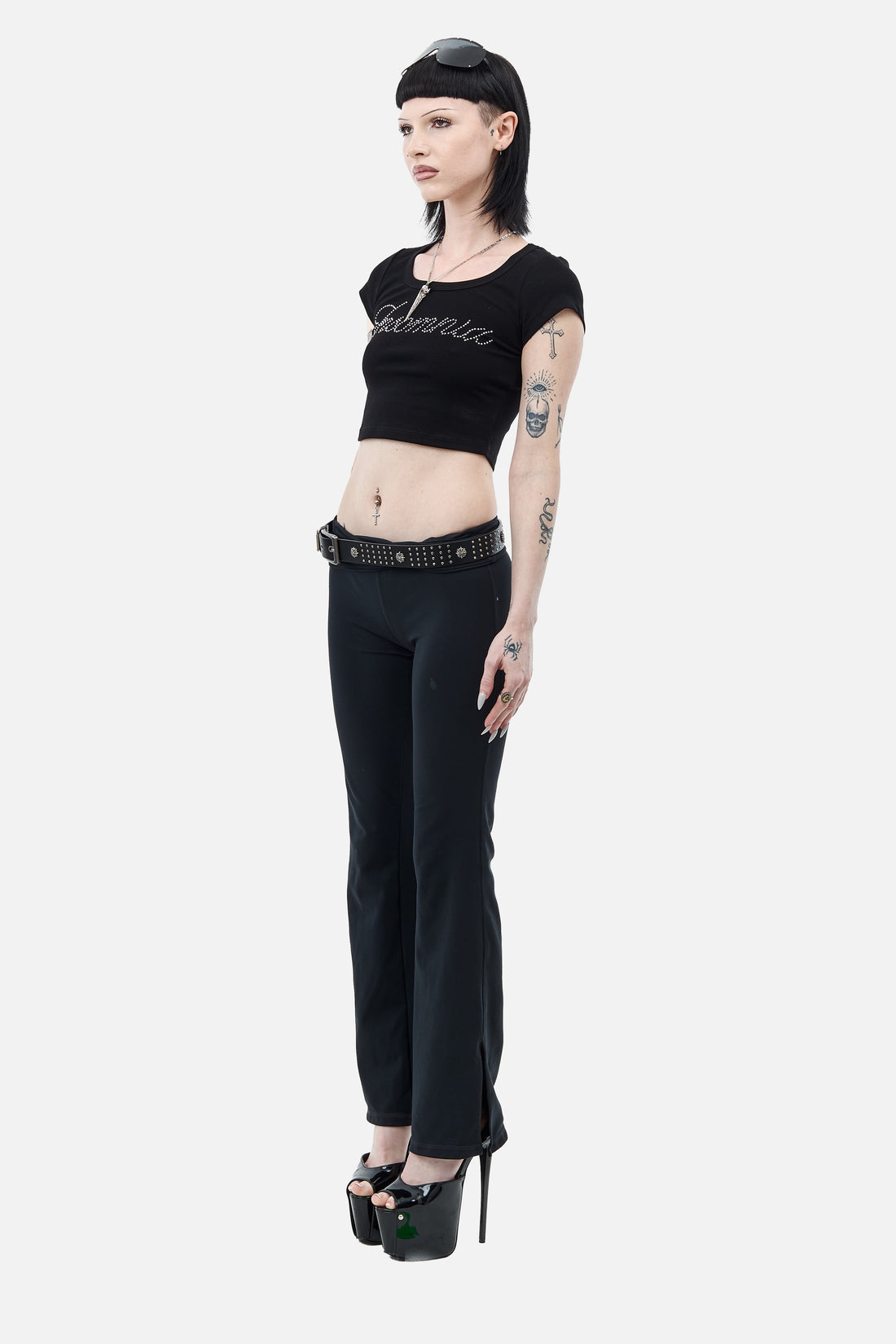 Side view of the cropped Rhinestone Cursive Tee worn with black flared pants and platforms