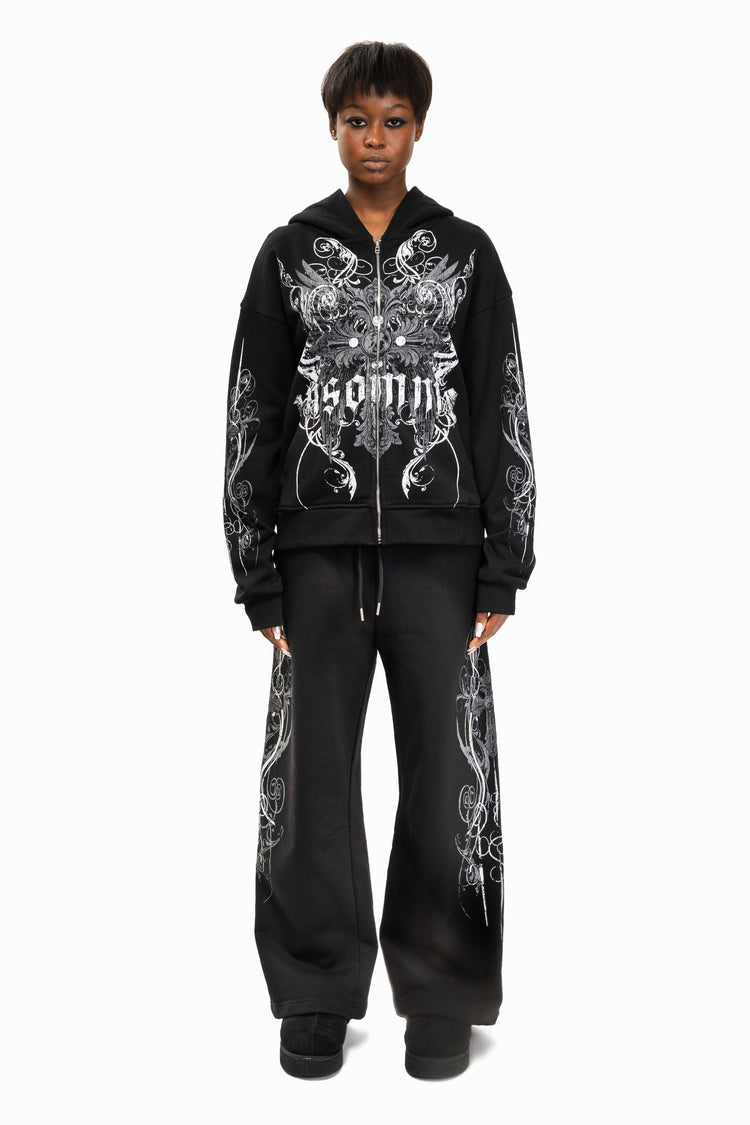 Model wearing the black Crux Hoodie with black wide-leg pants, full-length front view