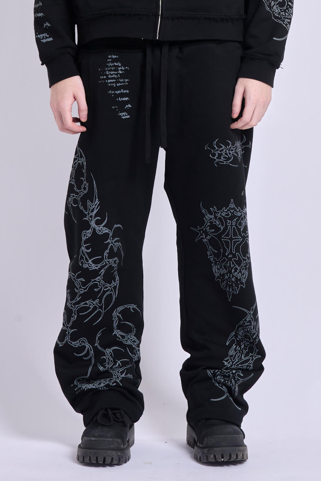 Front close-up of the Sigil Sweatpants showing the drawstring waist and silver tribal embroidery