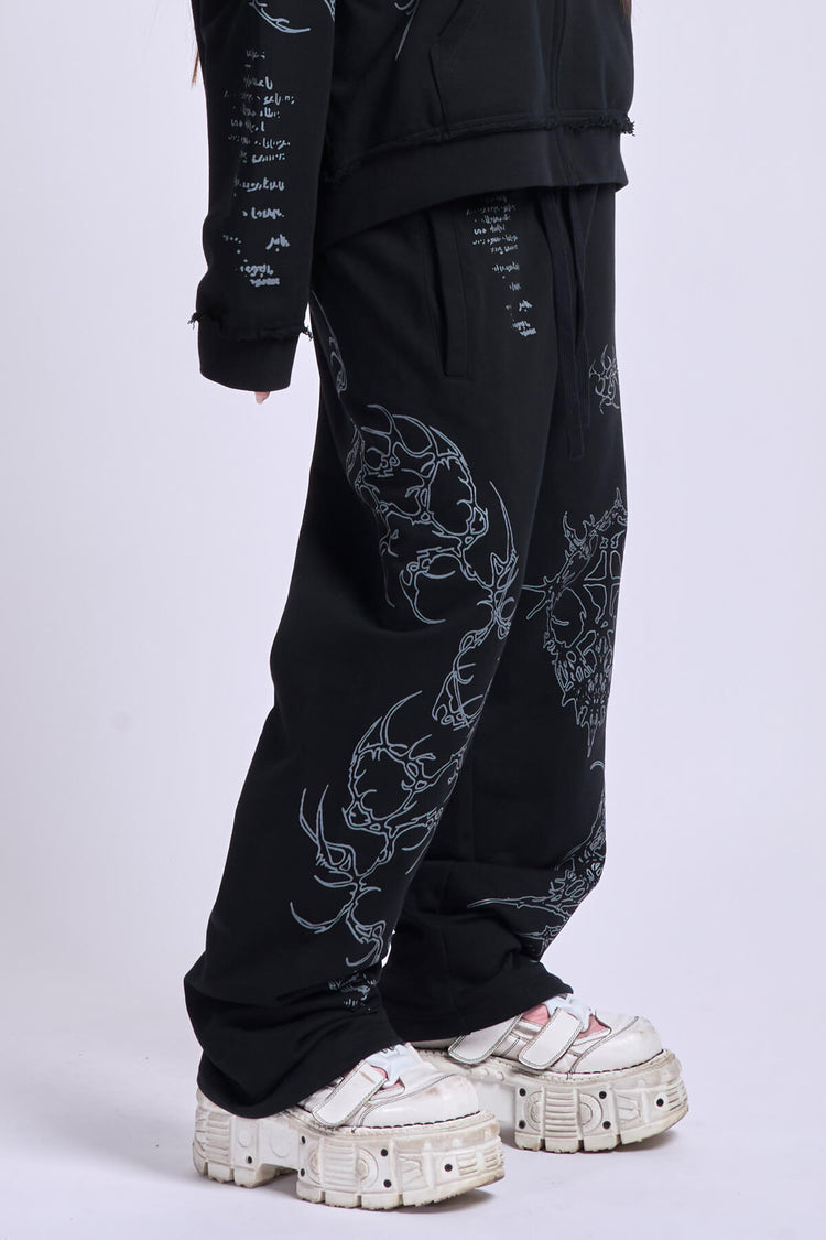 Side view of the black Sigil Sweatpants with silver tribal embroidery, styled with white platform sneakers
