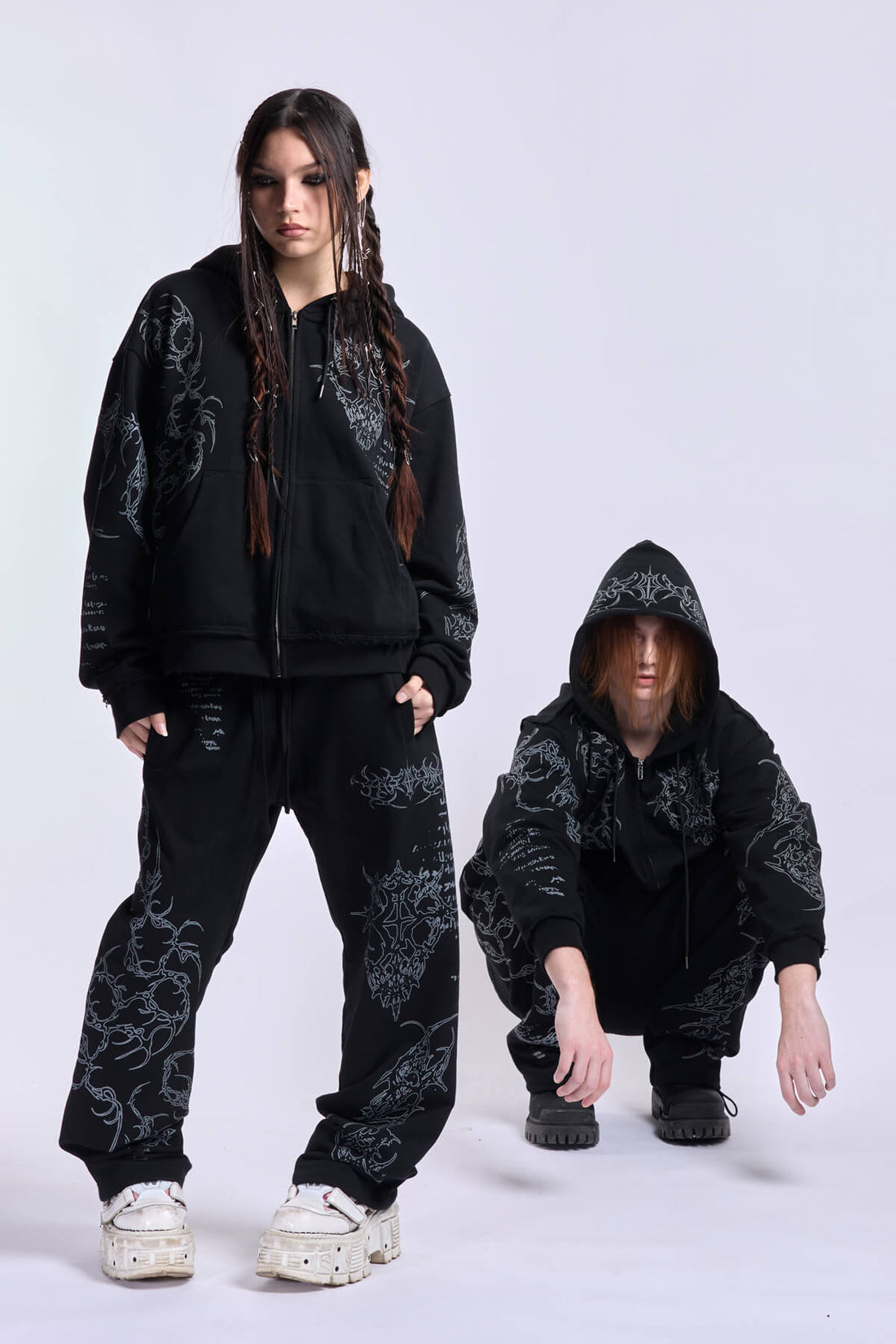 Two models in the matching Sigil sweatsuit, one standing and one crouching