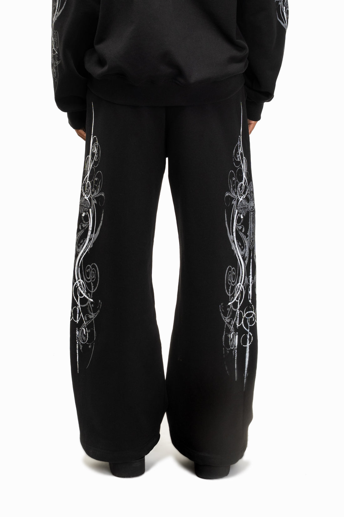 Back view of the Black Crux Sweatpants worn with matching hoodie, silver print down both legs