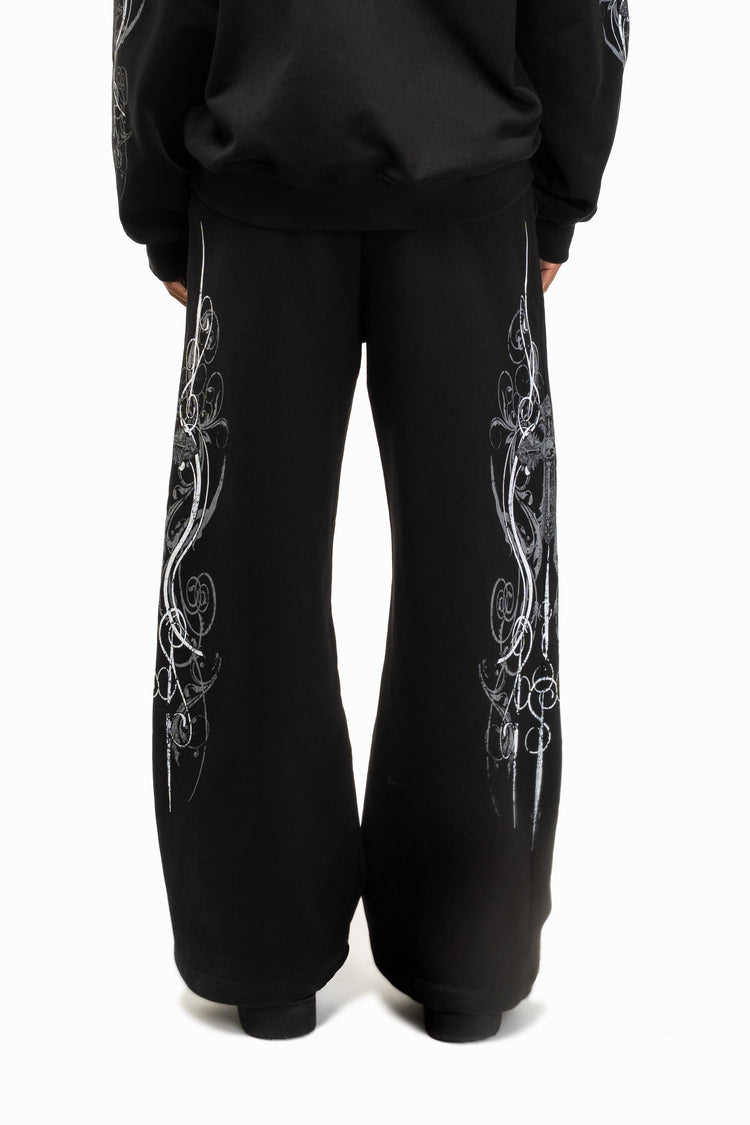 Back view of the Black Crux Sweatpants worn with matching hoodie, silver print down both legs