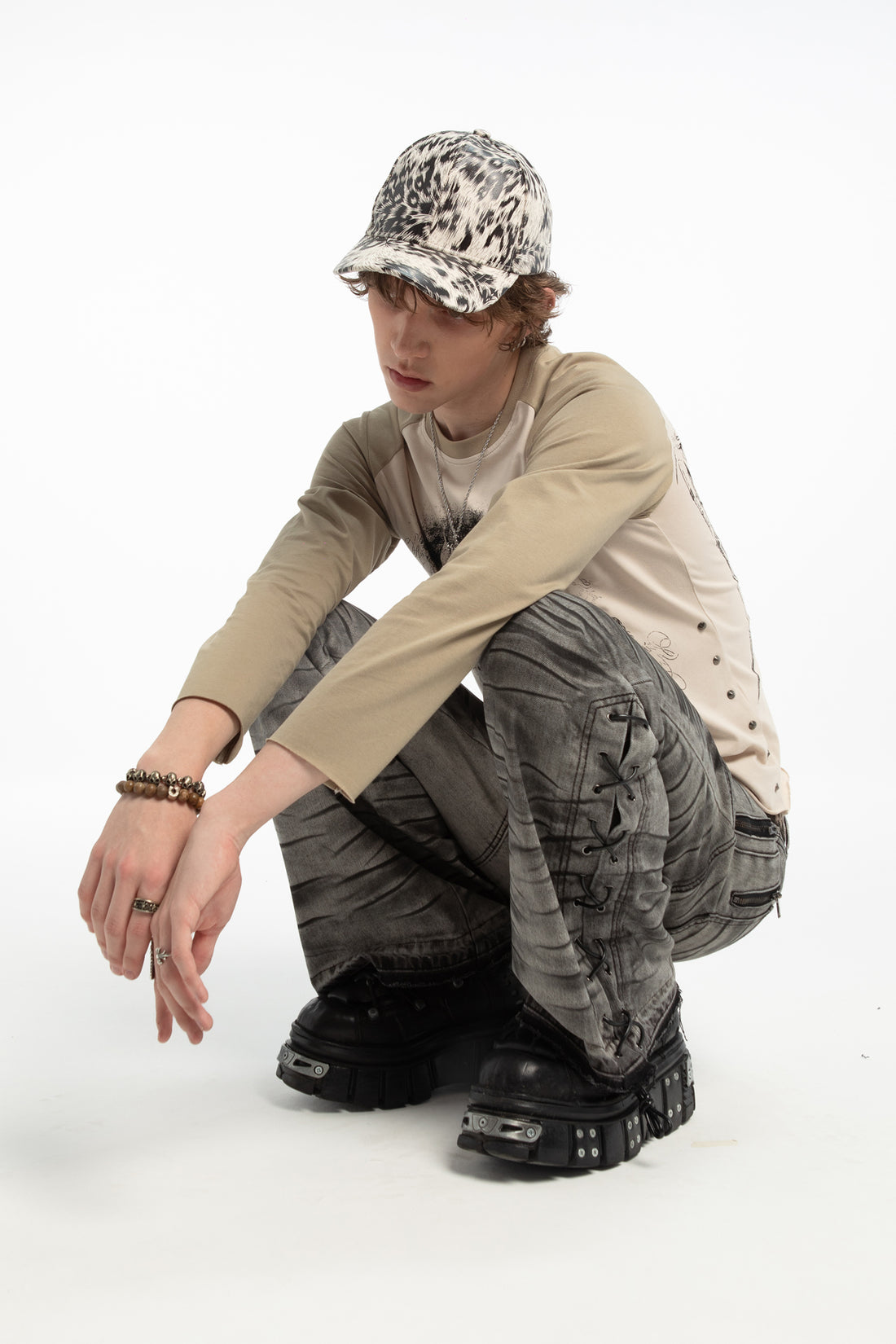 Model crouching in the White Cheetah Cap with laced grey jeans and platform boots