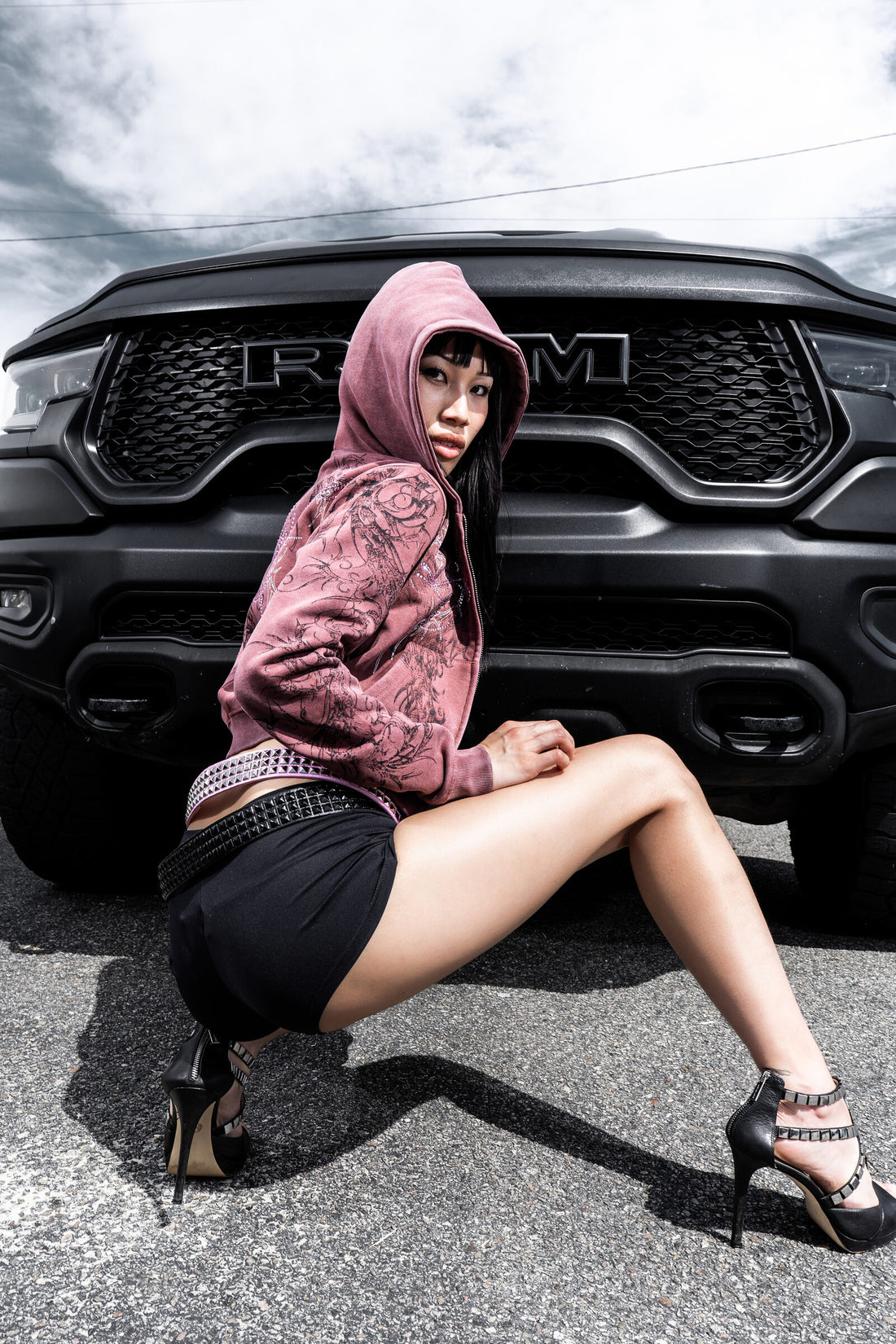 Model in the burgundy Fever Hoodie with hood up, crouching in front of a black truck