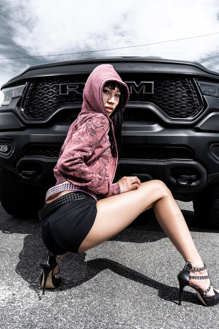 Model in the burgundy Fever Hoodie with hood up, crouching in front of a black truck