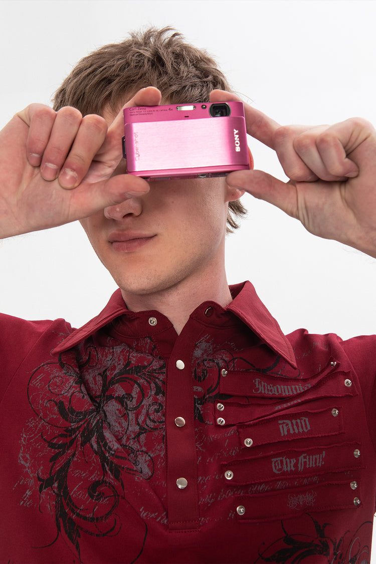Model holding a pink camera in front of his face in the Thorns Polo, studded chest detail