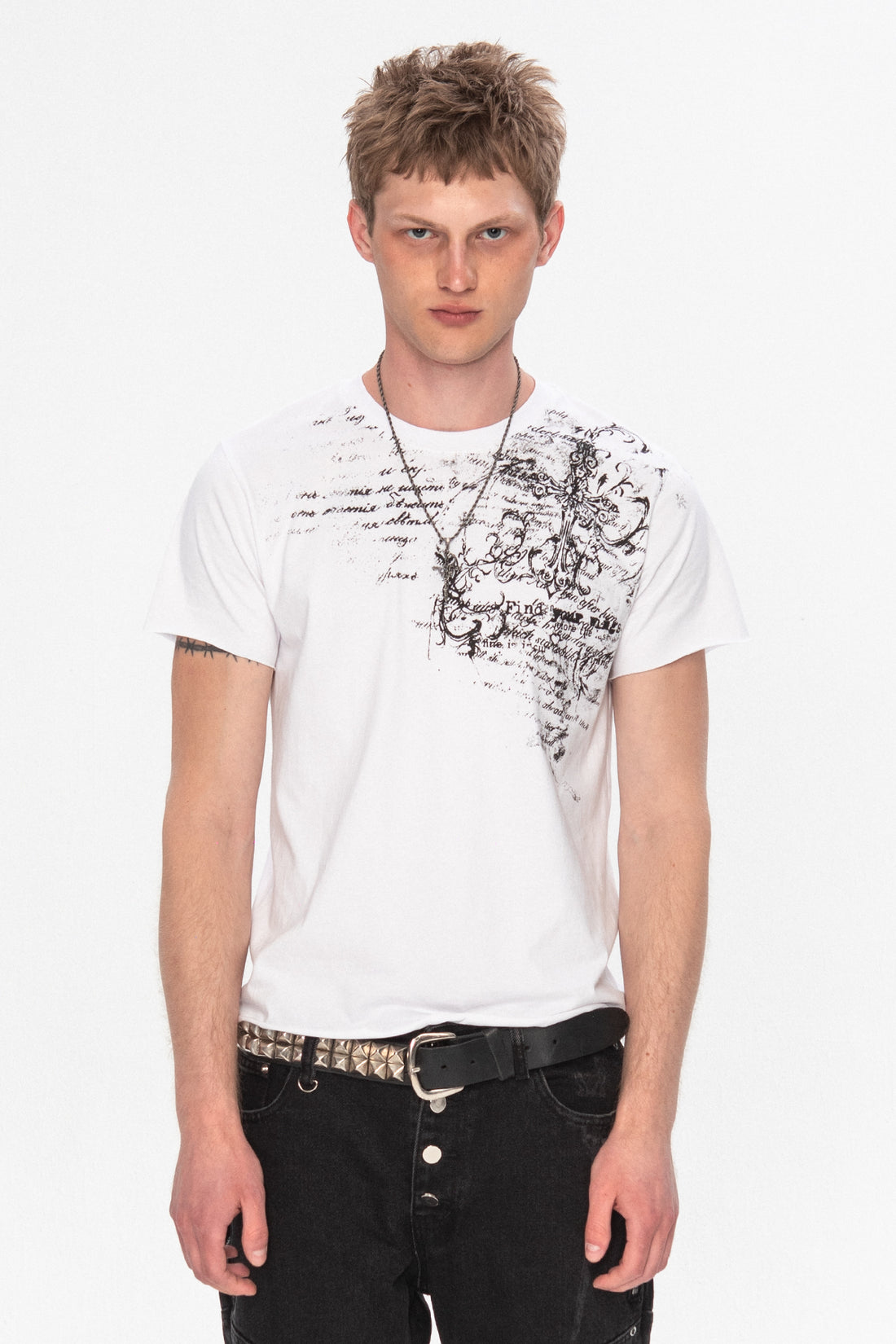 Model wearing the white Orison Tee with black script and cross print on one shoulder