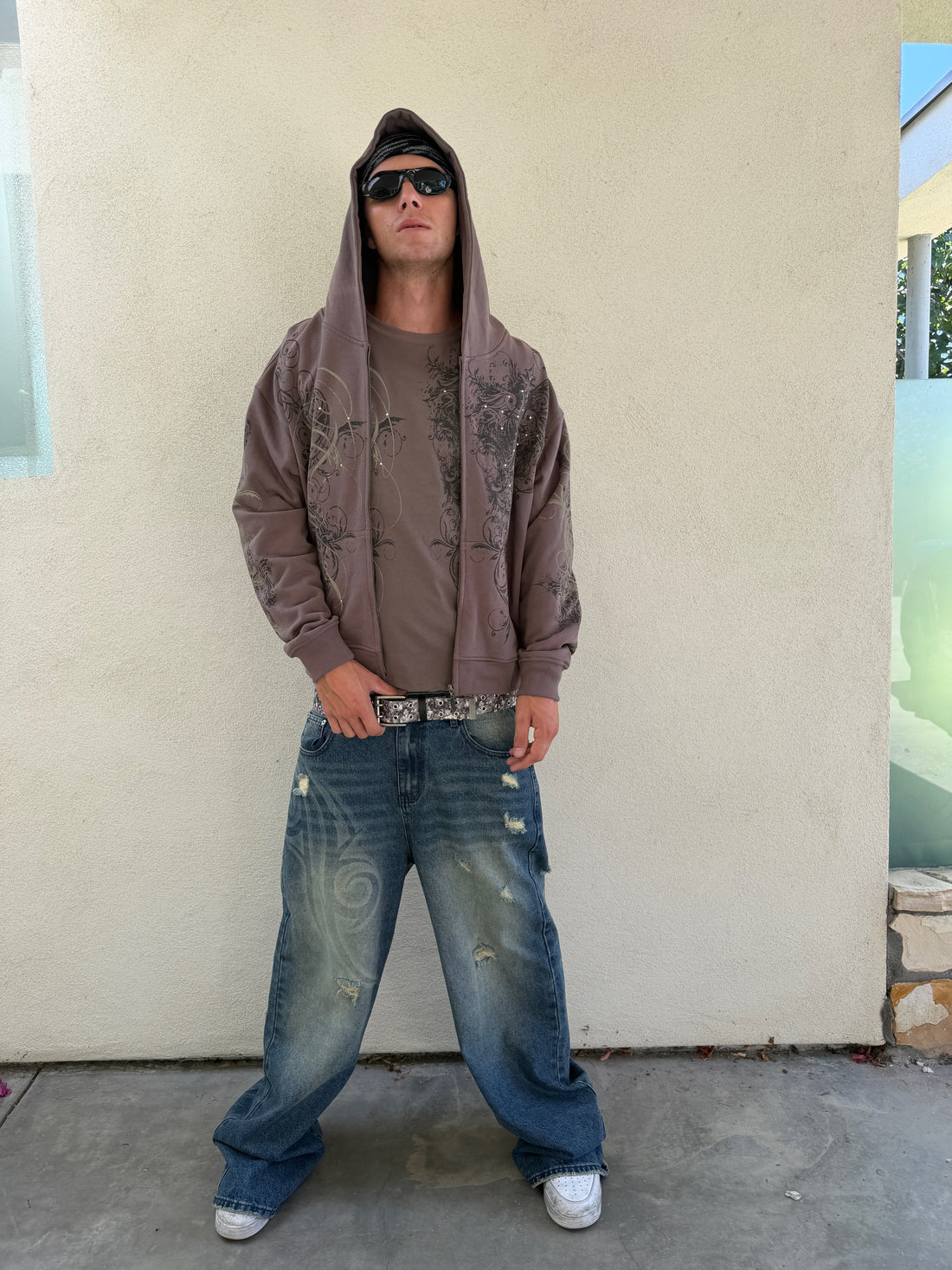 Model in sunglasses wearing the Brown Scripture Eclipse Zip Up Hoodie hood up with baggy jeans