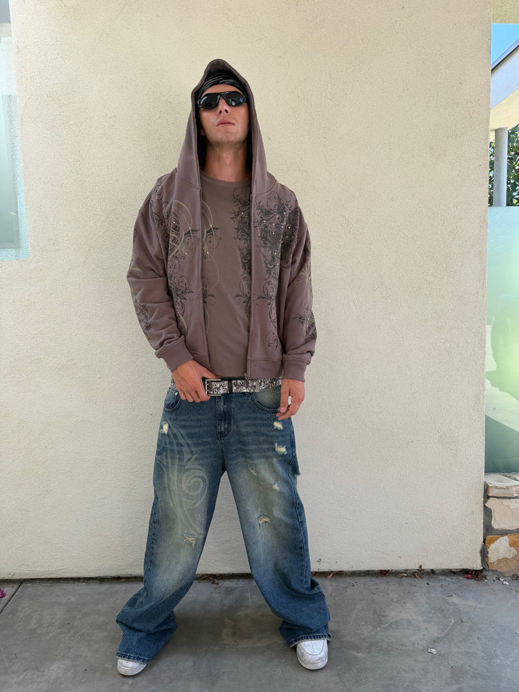 Model in sunglasses wearing the Brown Scripture Eclipse Zip Up Hoodie hood up with baggy jeans