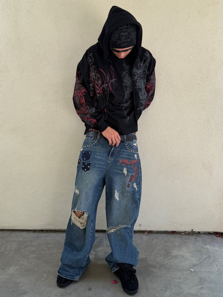 Model wearing the Black Scripture Eclipse Zip Up Hoodie hood up with ripped patched jeans outdoors