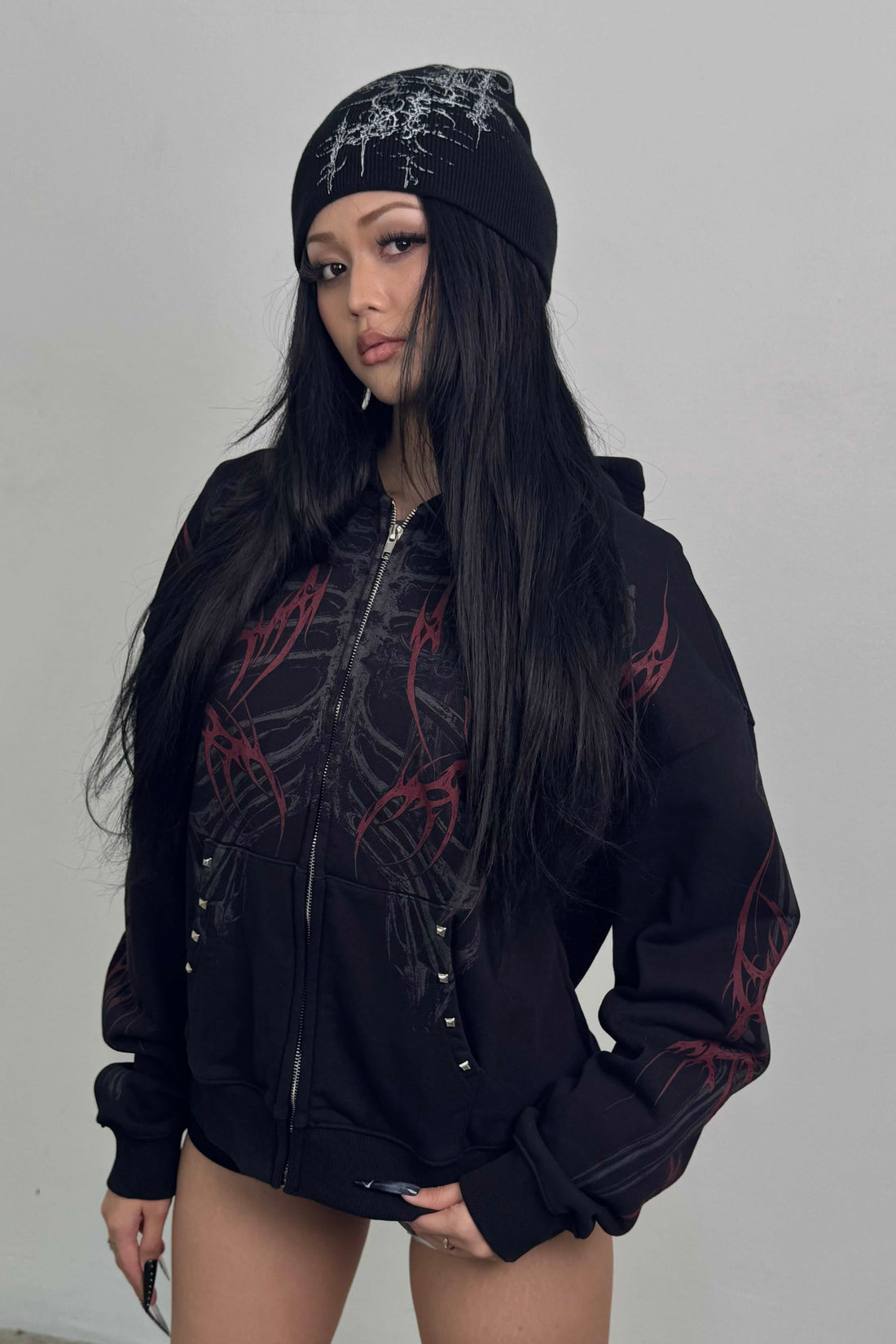 Model with long black hair in the zipped Skeleton Hoodie and a graphic beanie
