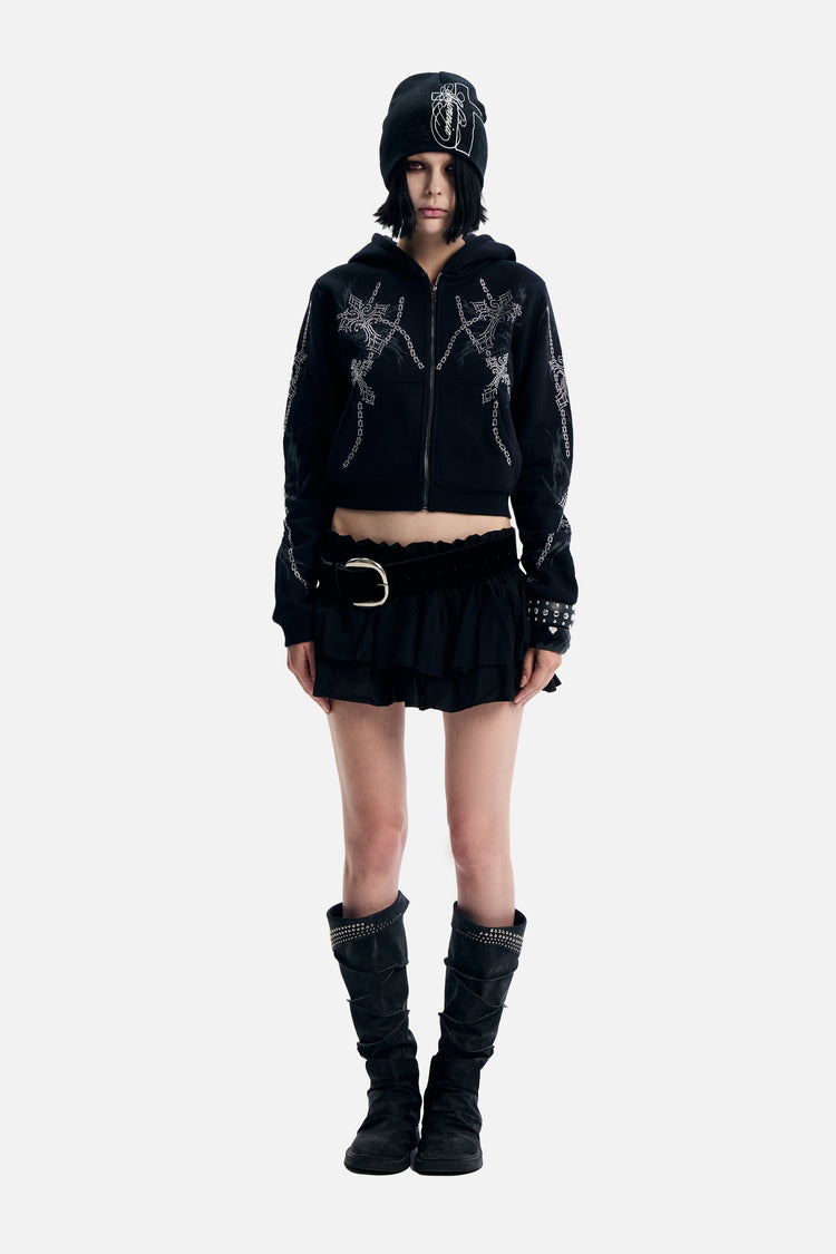 Model wearing the black Chain Rhinestone Hoodie cropped zip up with a ruffle mini skirt and boots, full length