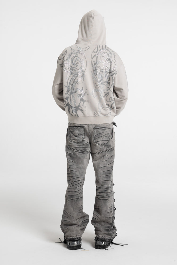 Back view of the Rhinestone Tribal Zip Hoodie with hood up and gray flared jeans, full-length
