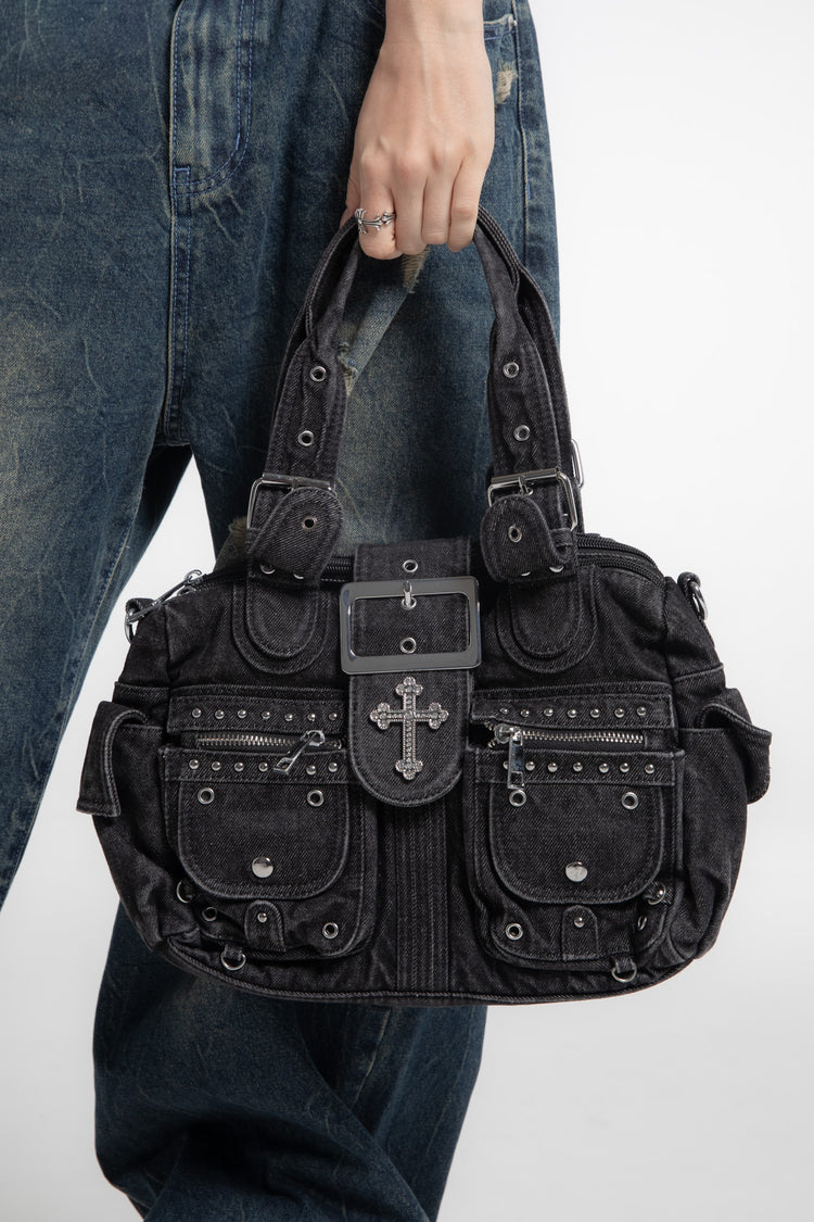 Hand carrying the Cross Denim Shoulder Bag by its top handles against faded jeans