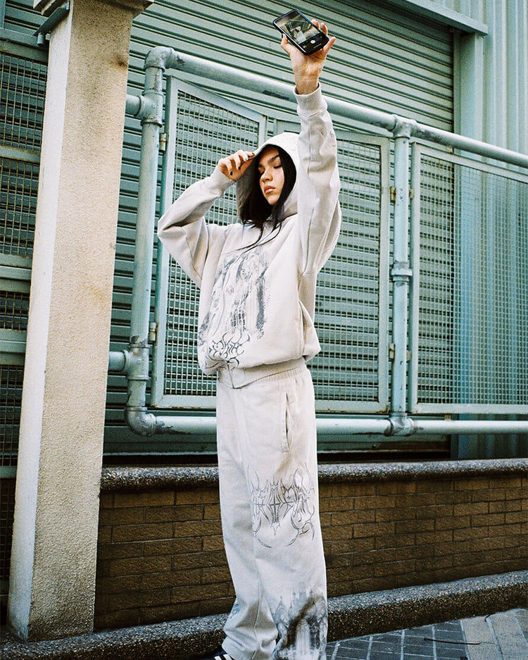 Model holding a phone overhead in the Gray Cathedral Sweatpants and matching hoodie outdoors
