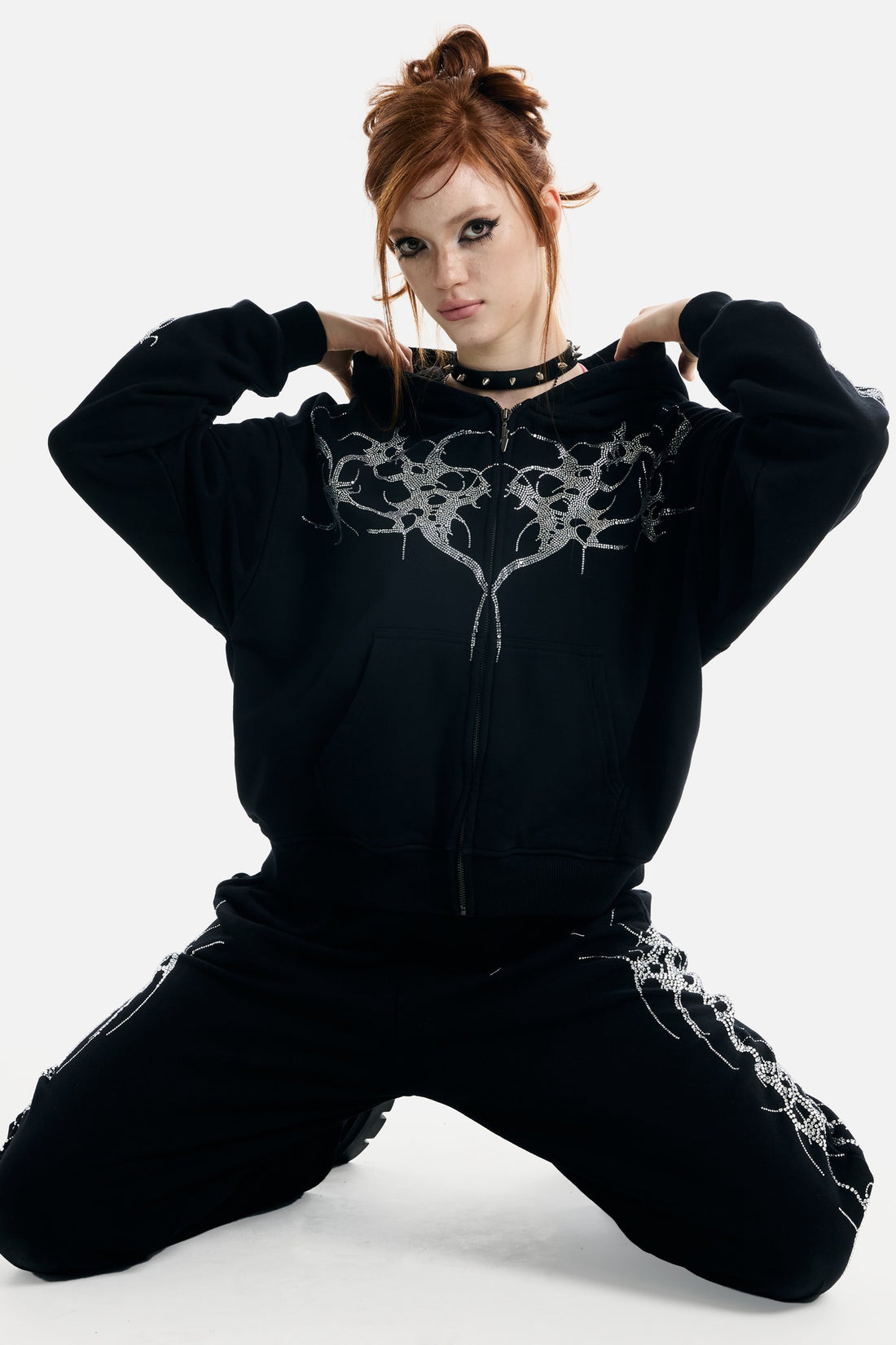 Model kneeling in the black Thorns Rhinestone Hoodie with hands at the hood