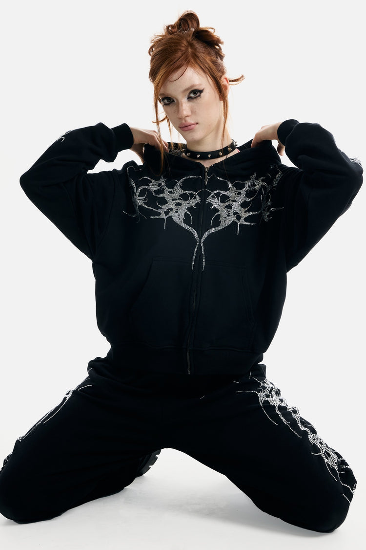 Model kneeling in the black Thorns Rhinestone Hoodie with hands at the hood