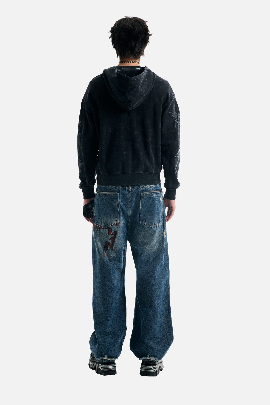 Full-length back view of the washed black Tribal Zip Up Hoodie with baggy patched jeans
