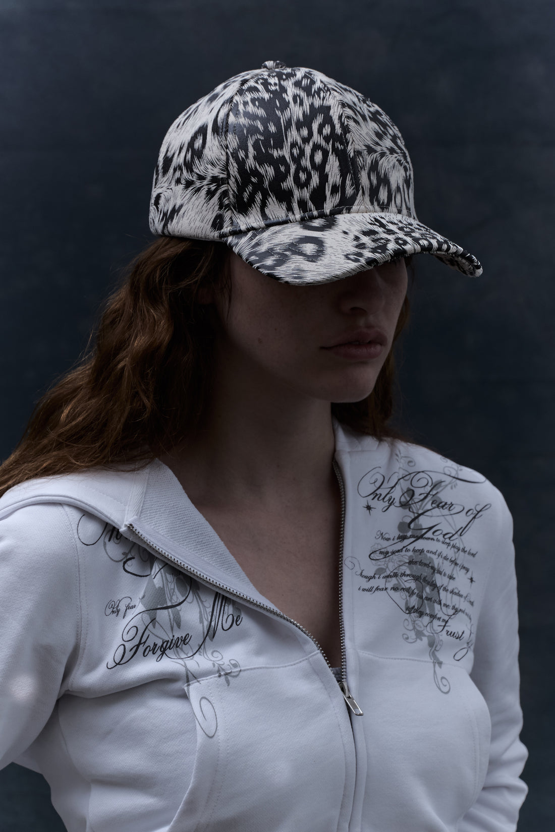 Long-haired model in the White Cheetah Cap with a white script zip hoodie